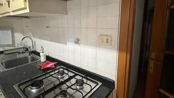 Een kleine keuken met een gasfornuis, een spoelbak en witte betegelde wanden.