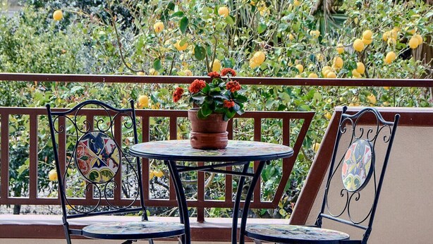 A balcony with a round table and two chairs, surrounded by lush greenery and yellow fruits. - Villa the Scent of Oranges (Eboli)
