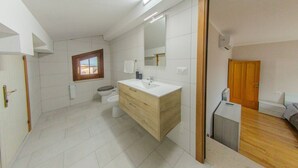 Een moderne badkamer met een houten wastafel, witte tegels, een raam en een zichtbare deur die naar een andere kamer leidt.