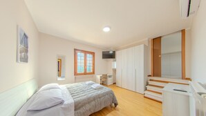 Een slaapkamer met een bed, een bureau, een kledingkast, een televisie en een raam.