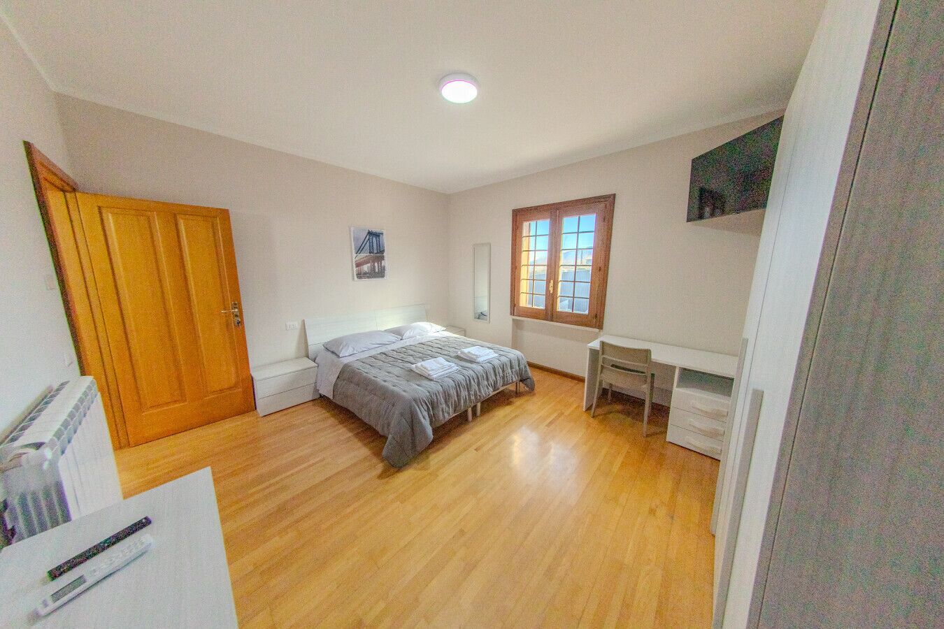 Ein Schlafzimmer mit Bett, Schreibtisch, Fenster und Tür.