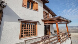 A two-story building with a balcony, wooden shutters, and a view of the landscape.