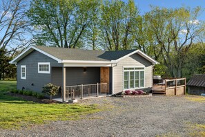 A small, single-story house with a covered porch, a wooden deck, and a barbecue area.