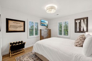 A bedroom with a large bed, a dresser, a TV on the wall, and framed pictures.