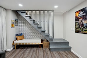 Eine Treppe mit grauer Geländer, eine Bank mit Kissen und ein Dinosaurier-Poster an der Wand.