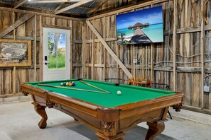 A pool table in a rustic room with wooden walls, a door, and a framed picture.