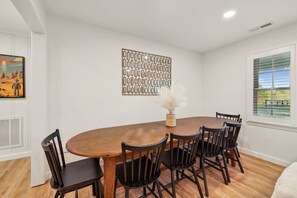 A dining area with a wooden table and chairs, a decorative wall piece, and a window with blinds.