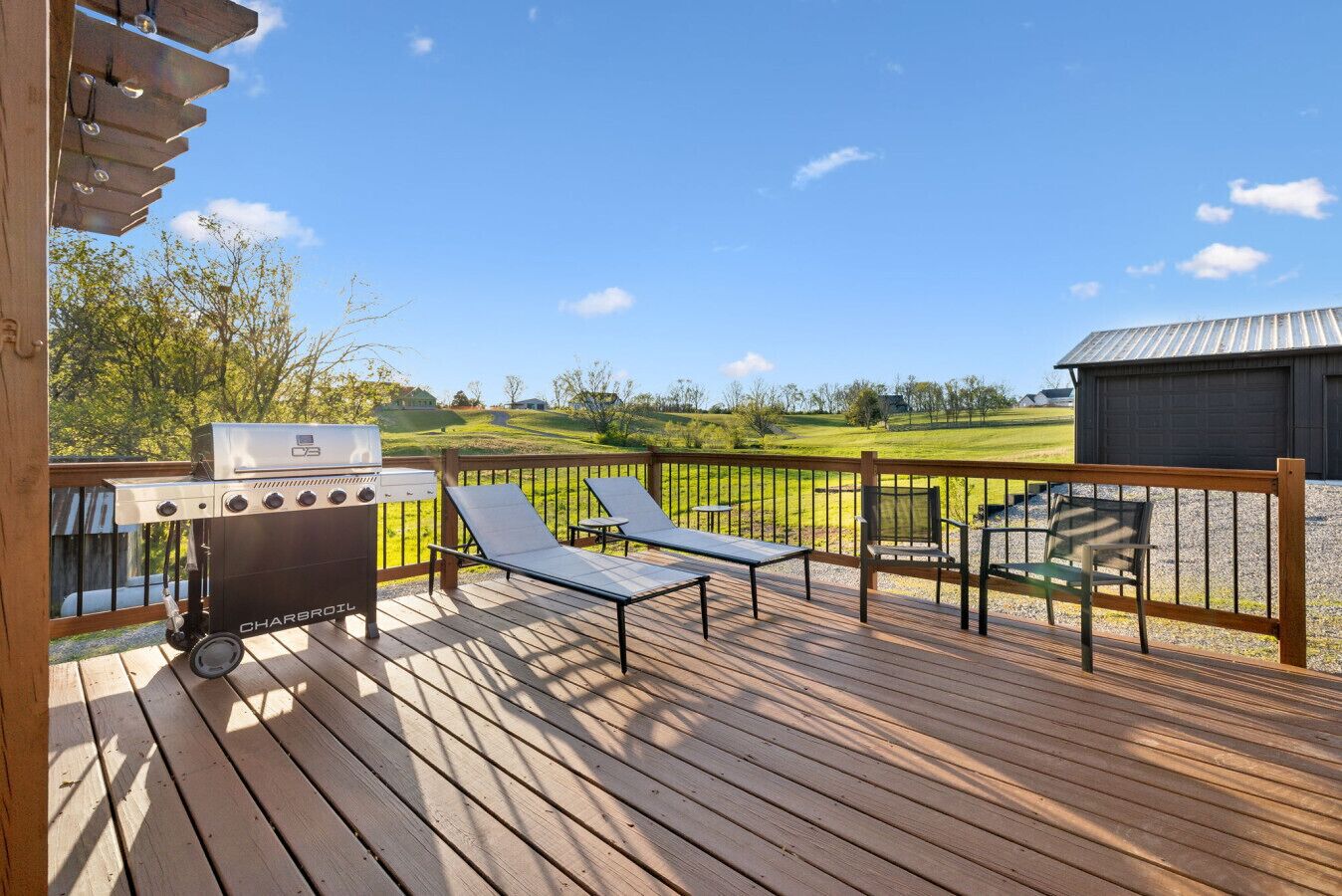 A wooden deck with a barbecue grill, lounge chairs, and a view of a green landscape.