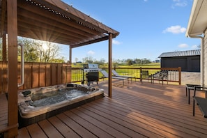 Eine Holzterrasse mit Whirlpool, Grill und Gartenmöbeln.