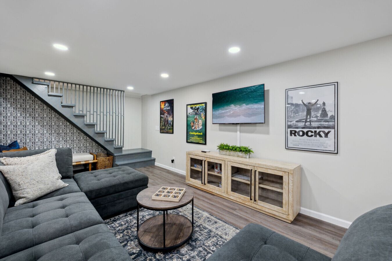 Ein modernes Wohnzimmer mit grauem Sofa, einem Couchtisch und einer Treppe mit einem gemusterten Wand.