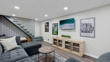 A modern living room with a grey sofa, a coffee table, and a staircase with a patterned wall.