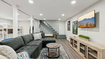 Una sala de estar moderna con un sofá seccional, una mesa de centro, un televisor montado en la pared y una escalera que conduce a otro nivel.