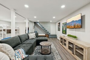 Una sala de estar moderna con un sofá seccional, una mesa de centro, un televisor montado en la pared y una escalera que conduce a otro nivel.