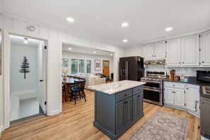 Una cocina moderna con armarios blancos, una isla central y un comedor con mesa y sillas de madera.