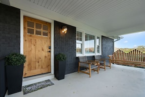 Eine überdachte Veranda mit einer Holztür, schwarzen Backsteinwänden und einer Bank.