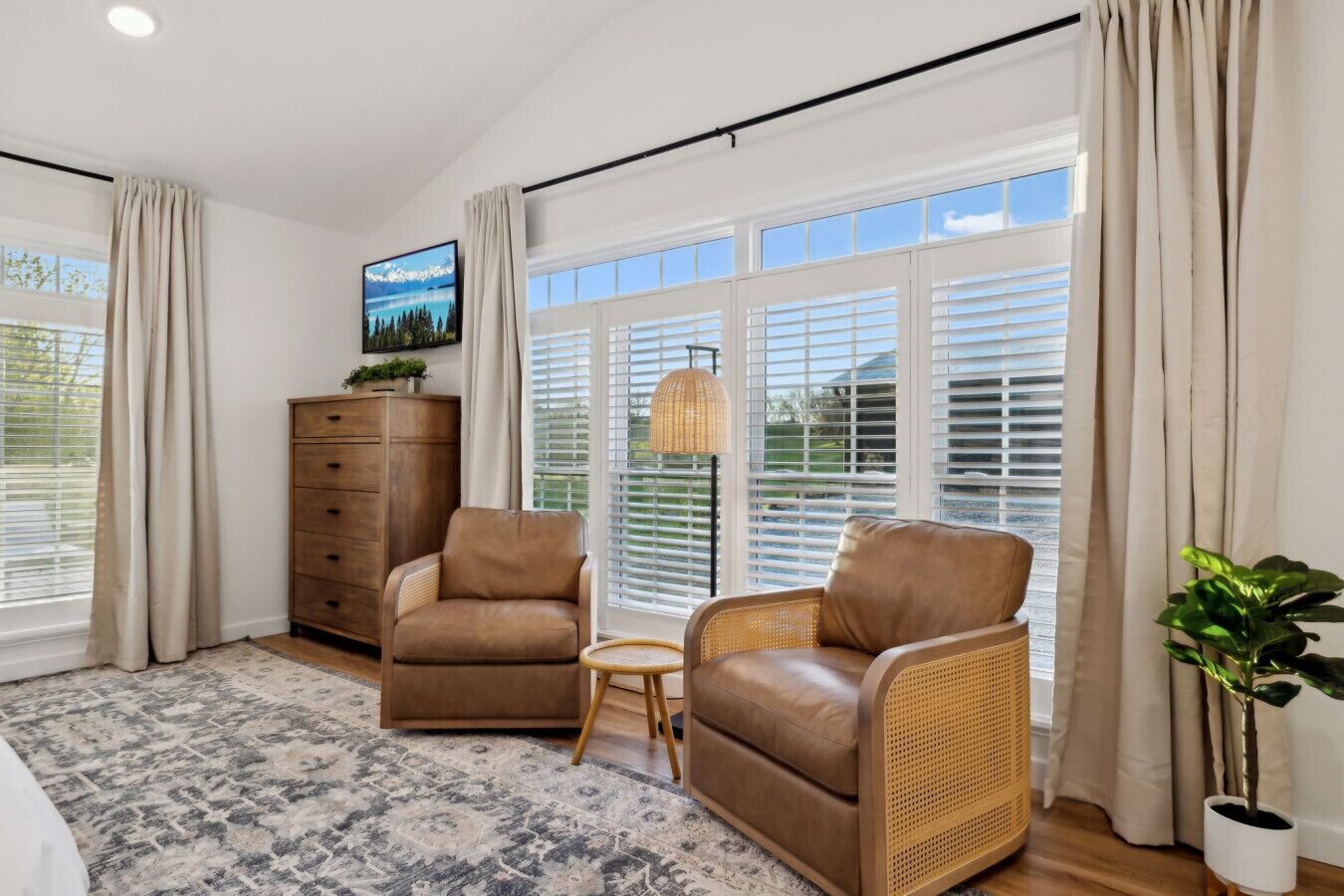 A spacious room with a large window, a sofa, a chair, a small table, a dresser, and a potted plant.