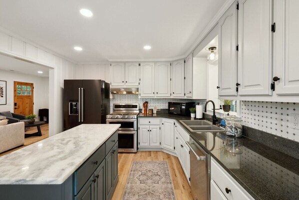 A modern kitchen with white cabinetry, stainless steel appliances, and a marble countertop.