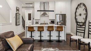 A modern kitchen with white cabinets, a stainless steel range hood, and a bar area with stools. - View of the City, Rooftop Patio, Games and More! (Nashville)