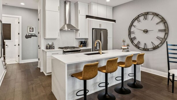 A modern kitchen with white cabinets, a stainless steel range hood, a large clock, and a bar area with stools. - View of the City, Rooftop Patio, Games and More! (Nashville)