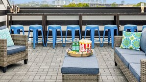 A rooftop terrace with wicker furniture, blue bar stools, and string lights. - View of the City, Rooftop Patio, Games and More! (Nashville)