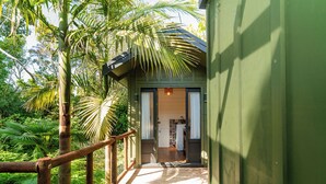 A wooden pathway leading to a small, green-roofed structure with a kitchen visible inside.
