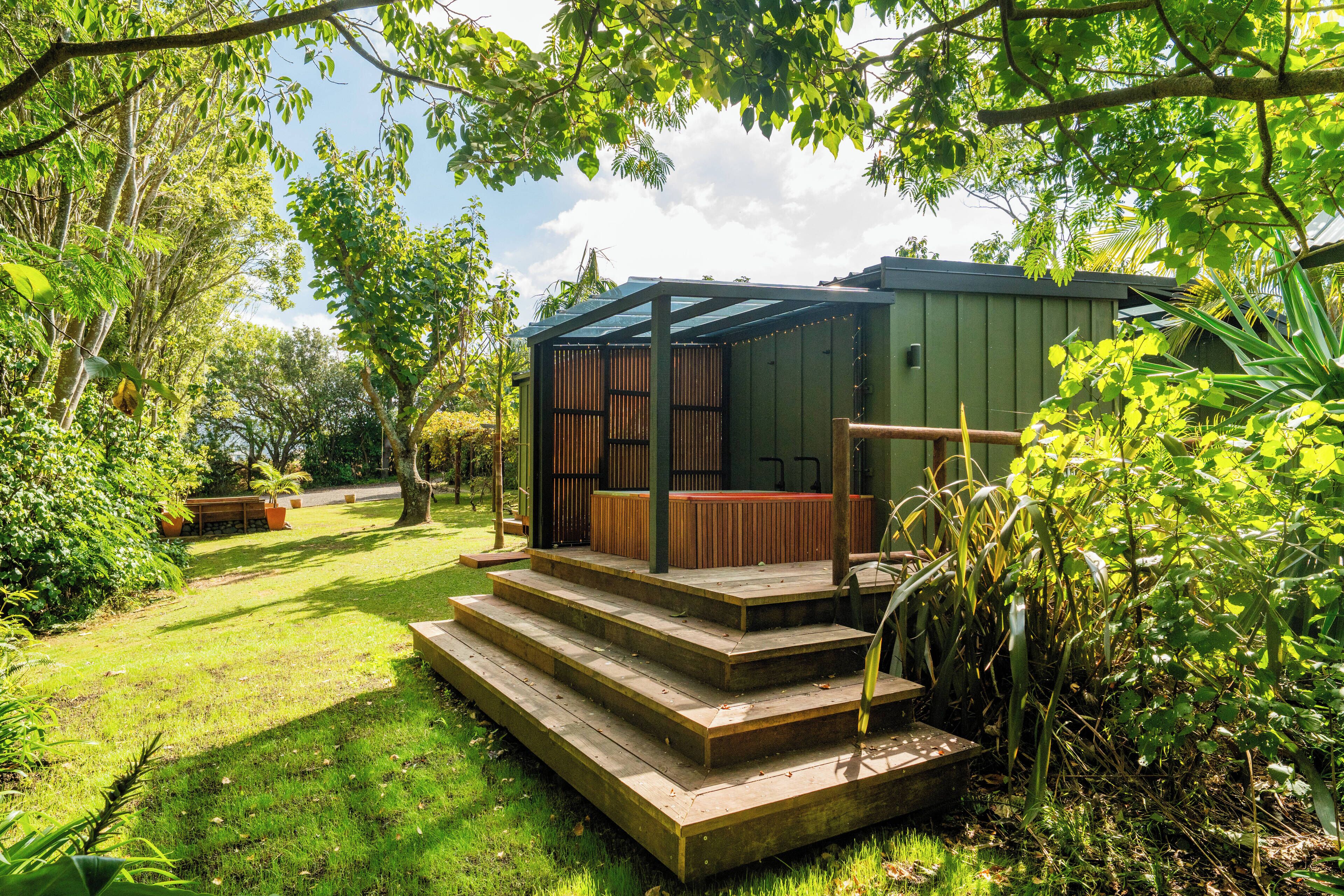 Une terrasse en bois mène à un espace extérieur abrité, agrémenté d’un banc et d’une petite table, le tout entouré d’une végétation luxuriante.