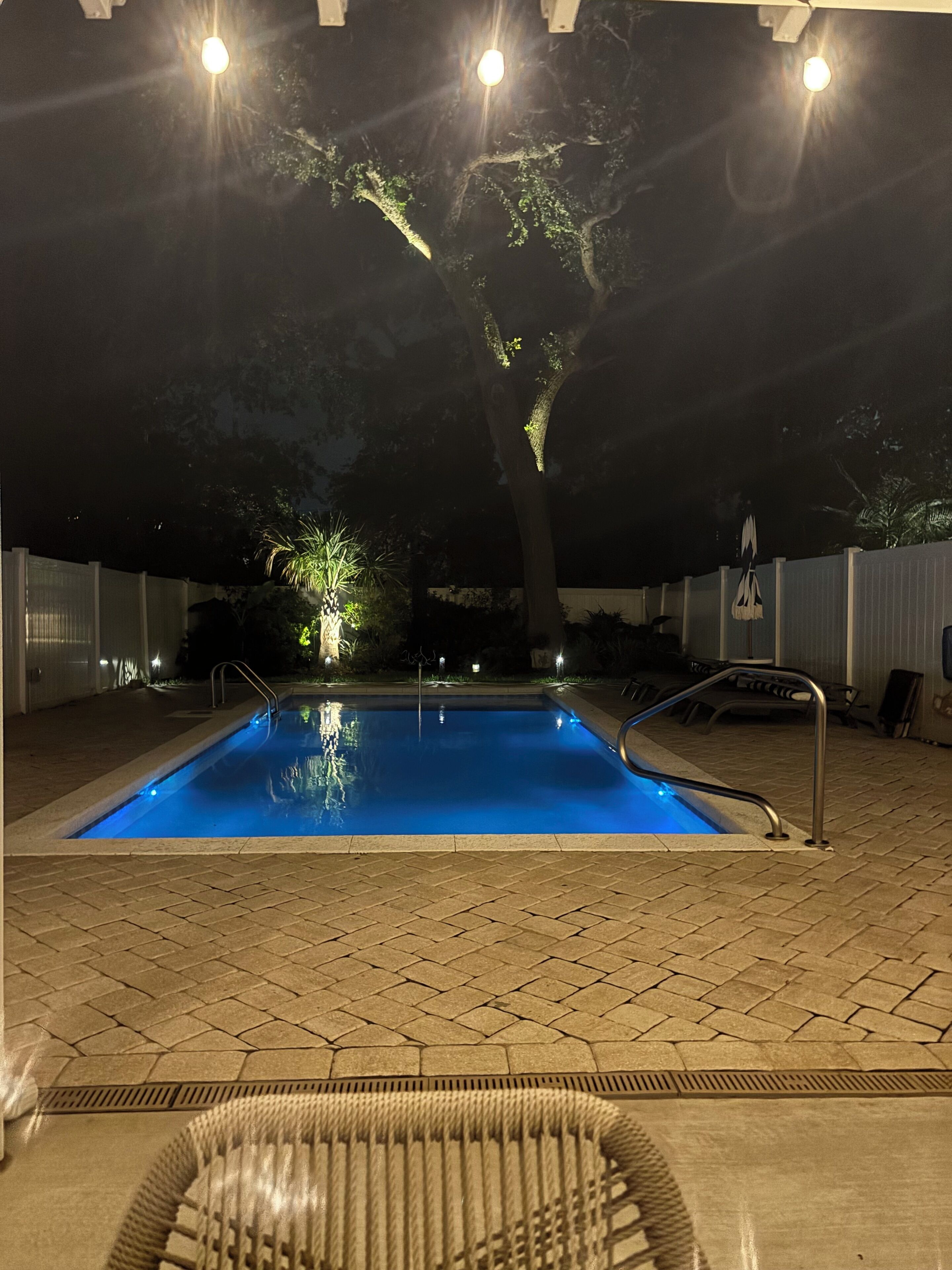 Una piscina con borde de baldosas, rodeada de una valla y árboles.