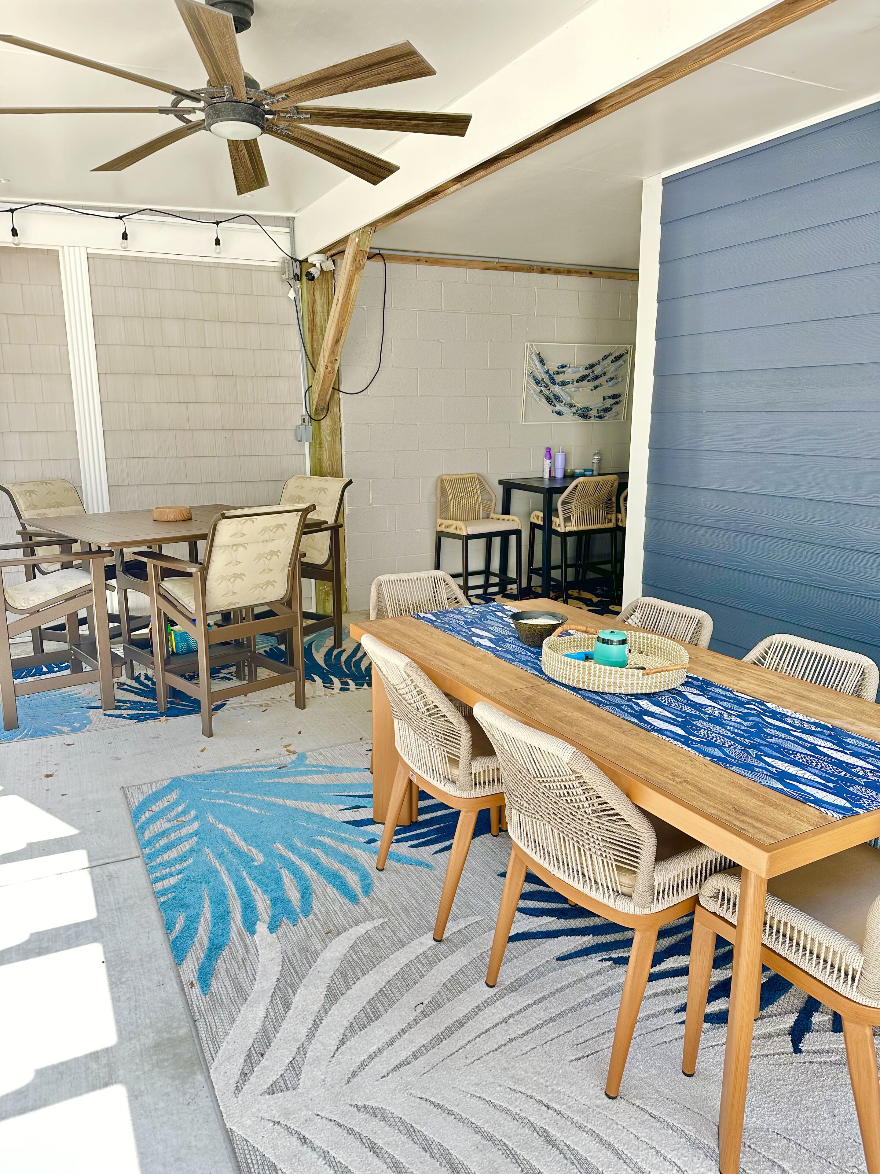 A dining area with a wooden table and wicker chairs, a ceiling fan, and a blue patterned rug.