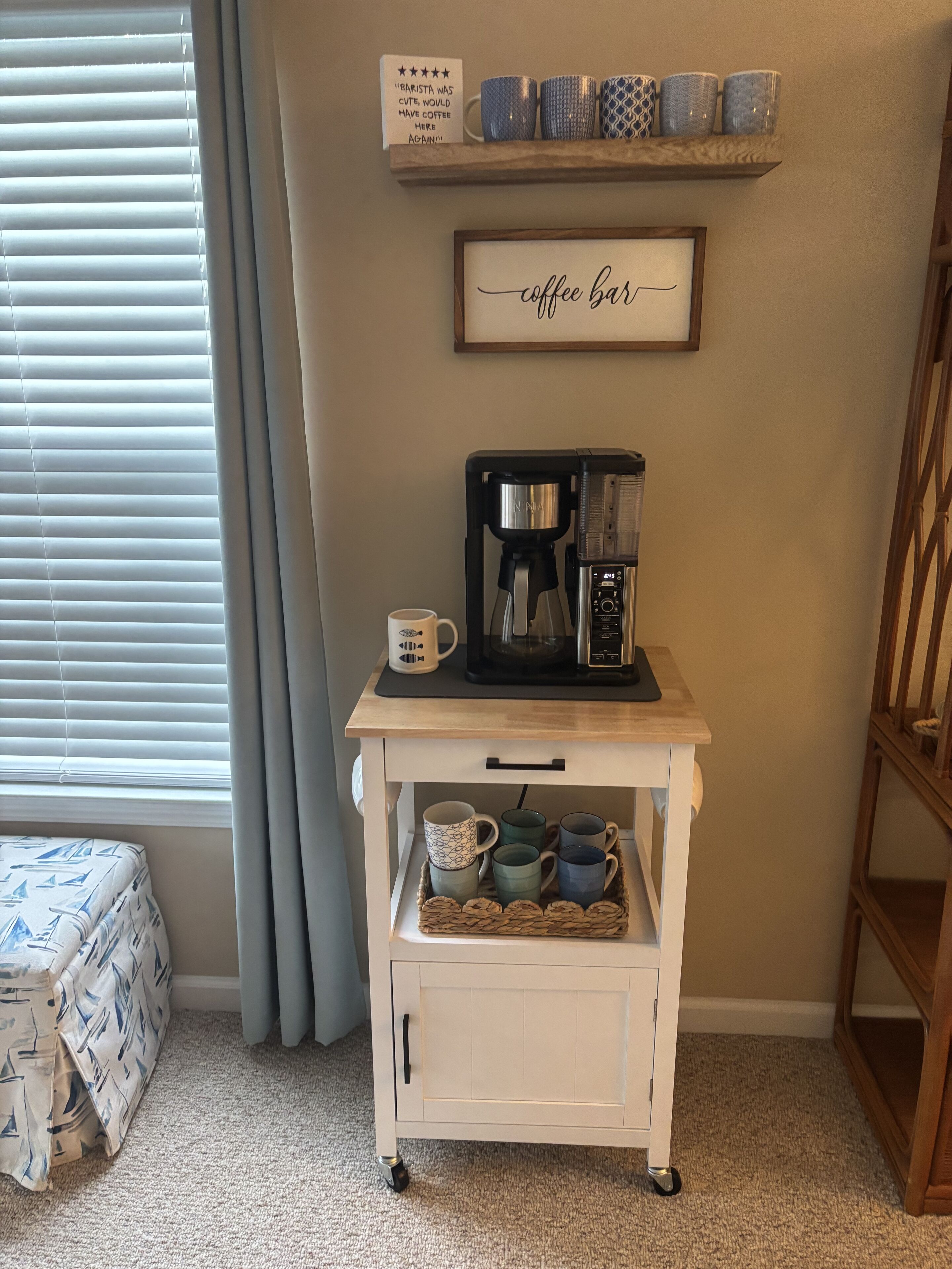 A coffee station with a coffee maker, mugs, and a sign above.