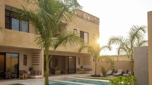 A modern building with a swimming pool, outdoor seating, and palm trees.