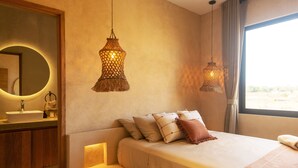 A modern bedroom with a large bed, bedside tables, a round mirror, and two hanging lamps.