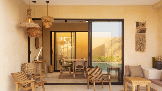 A modern living room with wooden furniture, a glass door leading to a balcony, and a woven wall hanging.