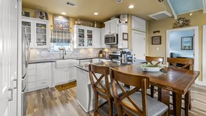 A kitchen with white cabinets, a wooden dining table, and a microwave. - Ocean View~Elevator~PetFriendly~Games~Beach Access (Bolivar Peninsula)