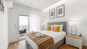 A modern hotel room with a large bed, two bedside tables, a balcony with a view, and a cityscape view. - Beautiful Sunset Views (Nazaré)