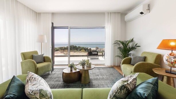 A modern living room with a green sofa set, two armchairs, a coffee table, and a view of the ocean through large sliding doors. - Beautiful Sunset Views (Nazaré)
