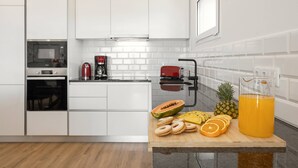 A modern kitchen with white cabinetry, a built-in oven, a coffee maker, and a fruit cutting board with sliced fruits and a pitcher of orange juice. - Beautiful Sunset Views (Nazaré)