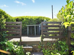 A wooden gate with a metal frame, surrounded by greenery and a clear sky.