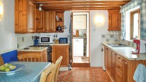 A kitchen with wooden cabinets, a microwave, a stove, a sink, and a dining area with a table and chairs. - Rivers View - UK49662 (Braunton)