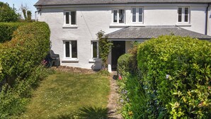A two-story house with a white exterior, a grey roof, and a small garden with a pathway leading to the entrance. - Rivers View - UK49662 (Braunton)
