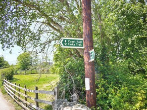 A wooden fence, a signpost with 'Coast Path Tarkra Trail' directions, and a stone wall.