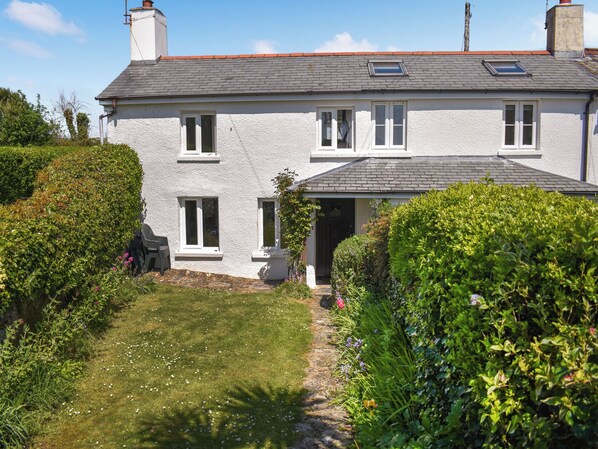 A two-story house with a white exterior, a grey roof, and a small garden with a pathway leading to the entrance.