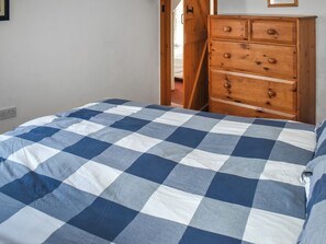 A bedroom with a checkered bedspread, a wooden dresser, and a door leading to another room.