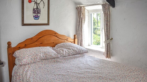 A bed with floral bedding, a wooden headboard, a window with curtains, and a framed artwork on the wall. - Rivers View - UK49662 (Braunton)