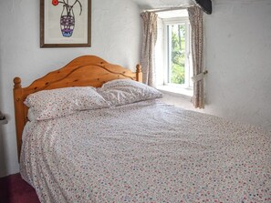 A bed with floral bedding, a wooden headboard, a window with curtains, and a framed artwork on the wall.