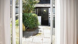 A narrow pathway leading to a building with a black door, surrounded by greenery and a stone-paved area. - Rivers View - UK49662 (Braunton)