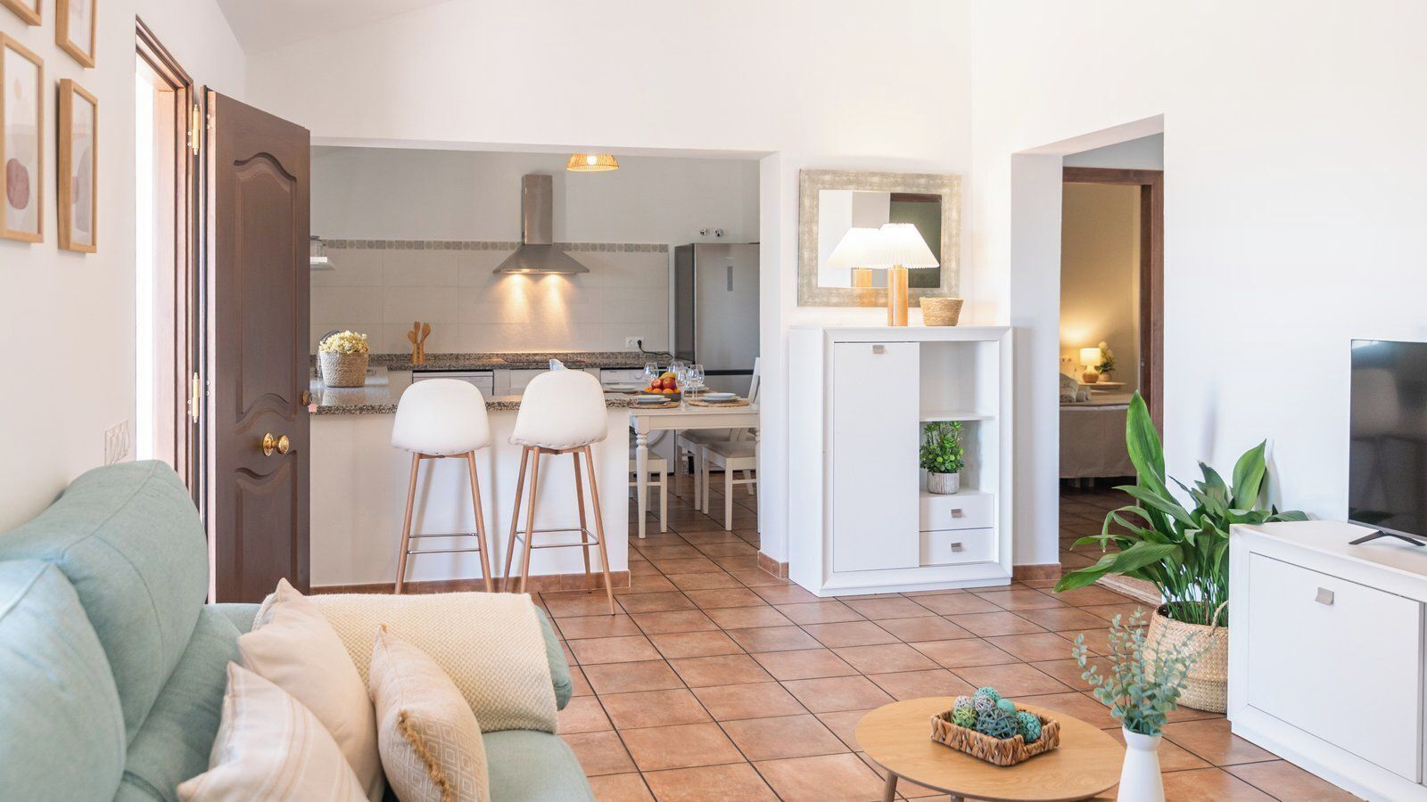Un salon moderne avec un canapé, deux fauteuils blancs, une table basse et un téléviseur.