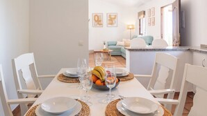 Un coin repas avec une table dressée pour quatre personnes, comprenant des assiettes, des verres et un saladier de fruits.