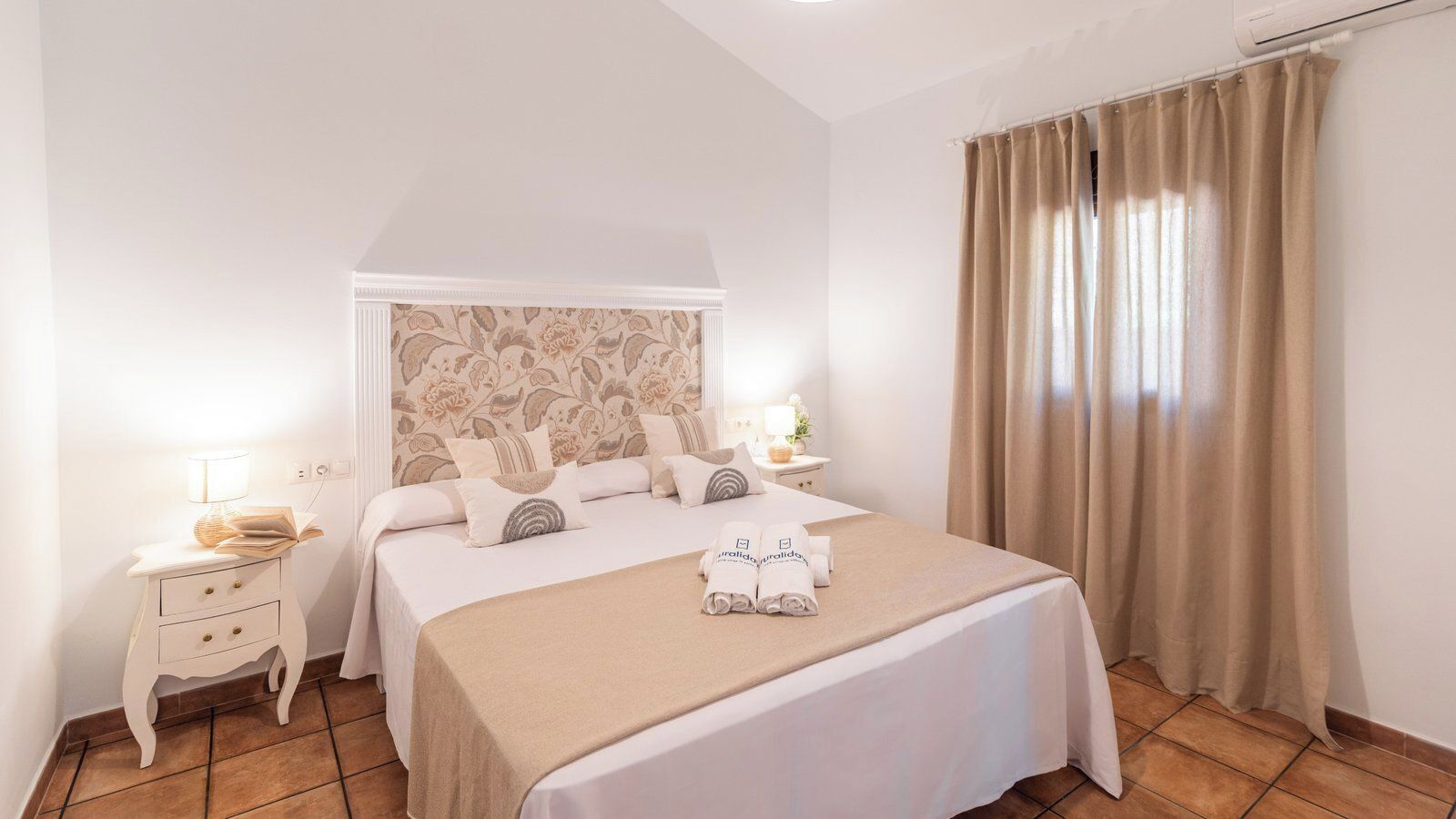 Une chambre d’hôtel avec un grand lit, une table de chevet avec une lampe et une fenêtre avec des rideaux.