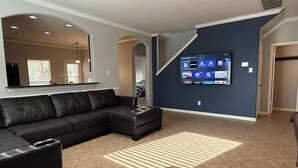 Un saló modern amb un sofà modular, un televisor de pantalla plana fixat a la paret i una escala que condueix a un altre pis.