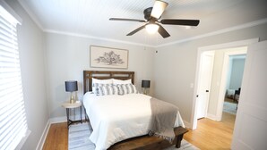 Ein Schlafzimmer mit einem Bett, zwei Nachttischen, einem Deckenventilator und einer Tür zu einem anderen Raum.